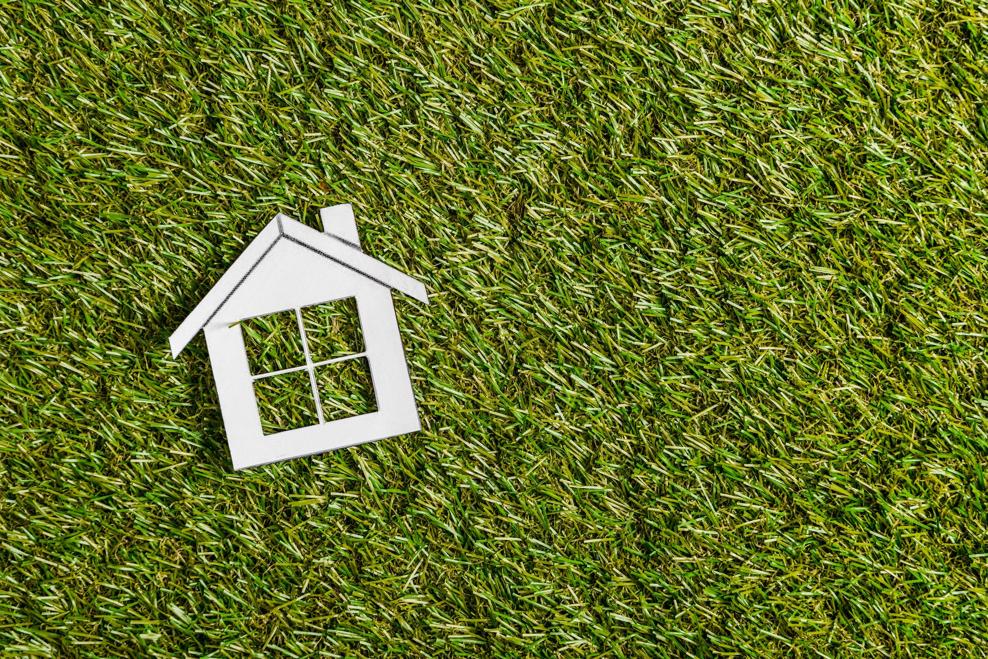 top view of white paper house on green grass, energy efficiency at home concept